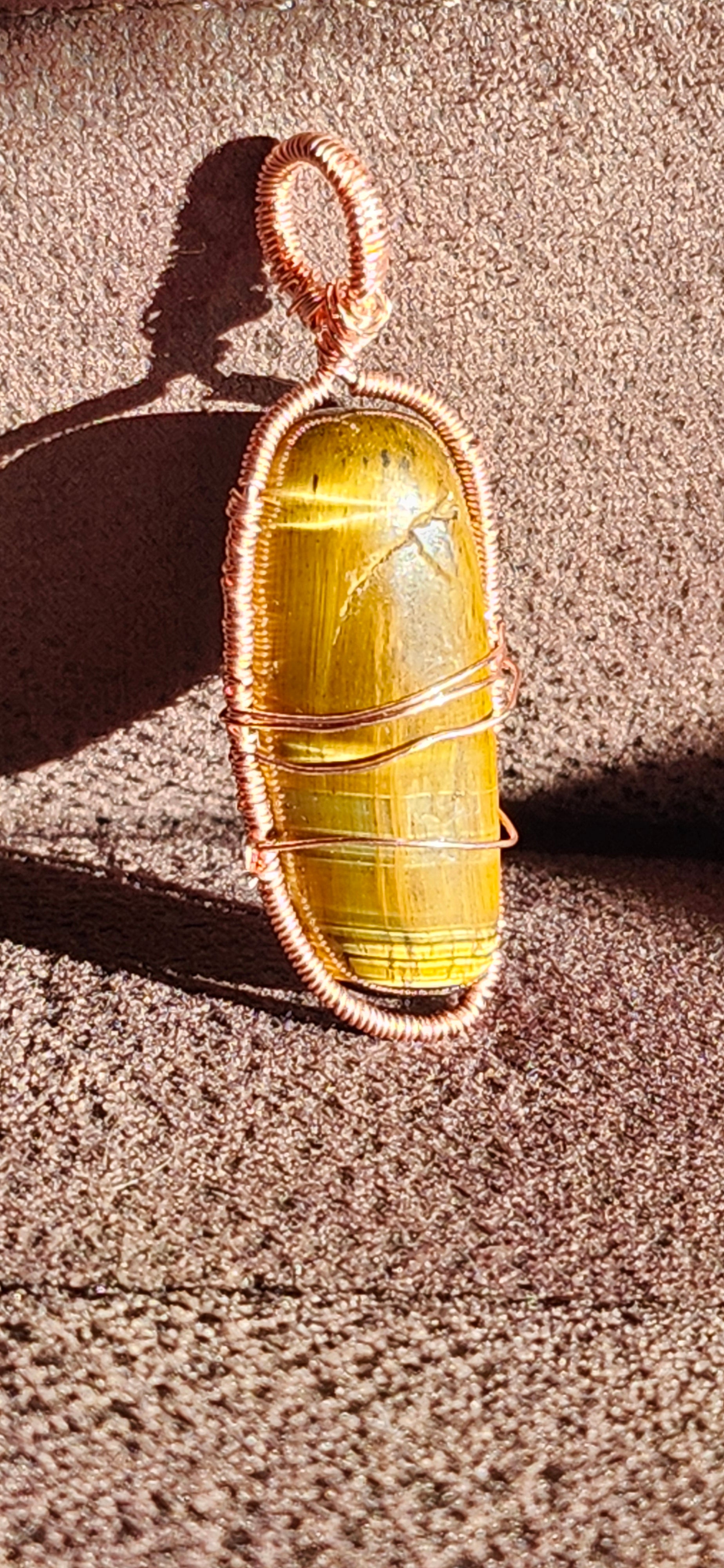 A copper wire wrapped tiger's eye pendant necklace laid out on a flat surface, displaying the yellow-gold stone with the metallic copper wiring.