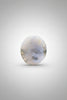 A smooth, polished white stone with natural cloudy inclusions, resting on a dark brown wooden tabletop.