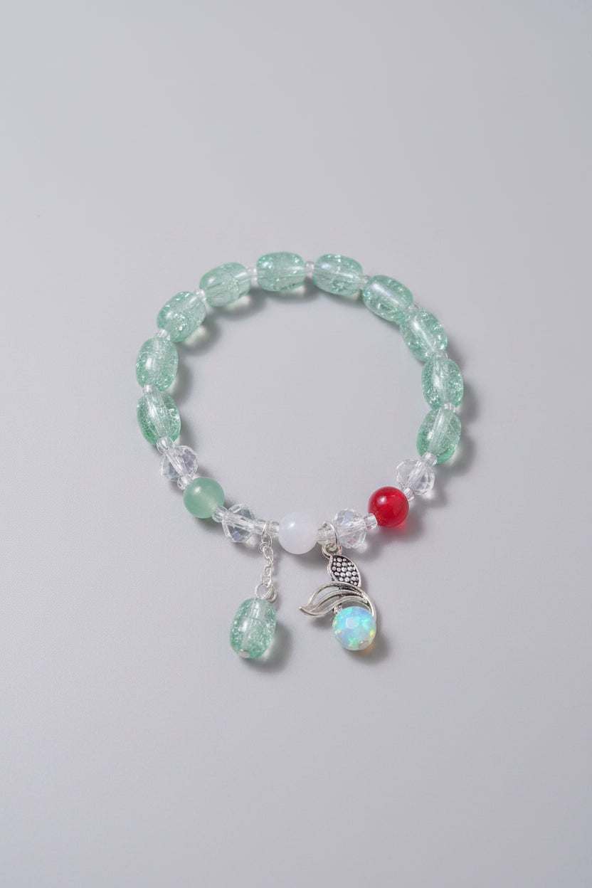 Green beaded bracelet with a red charm and silver accents on a gray background