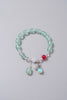 Green beaded bracelet with a red charm and silver accents on a gray background