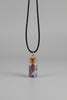 A small clear glass vial with a cork stopper and a black cord, photographed against a pale purple surface.